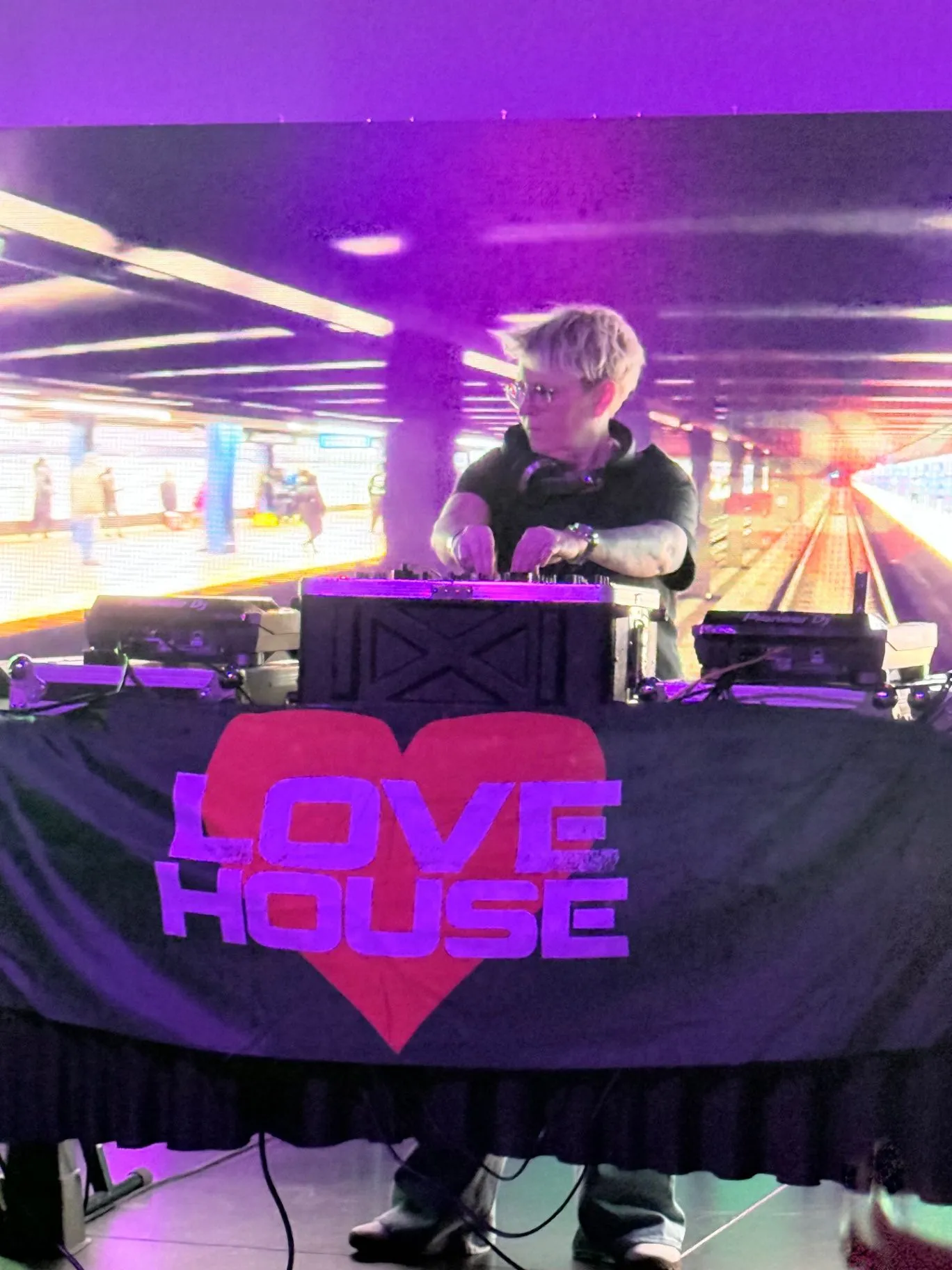 A DJ mixes on Pioneer decks behind a Love House heart-logo table cover with an LED screen behind.