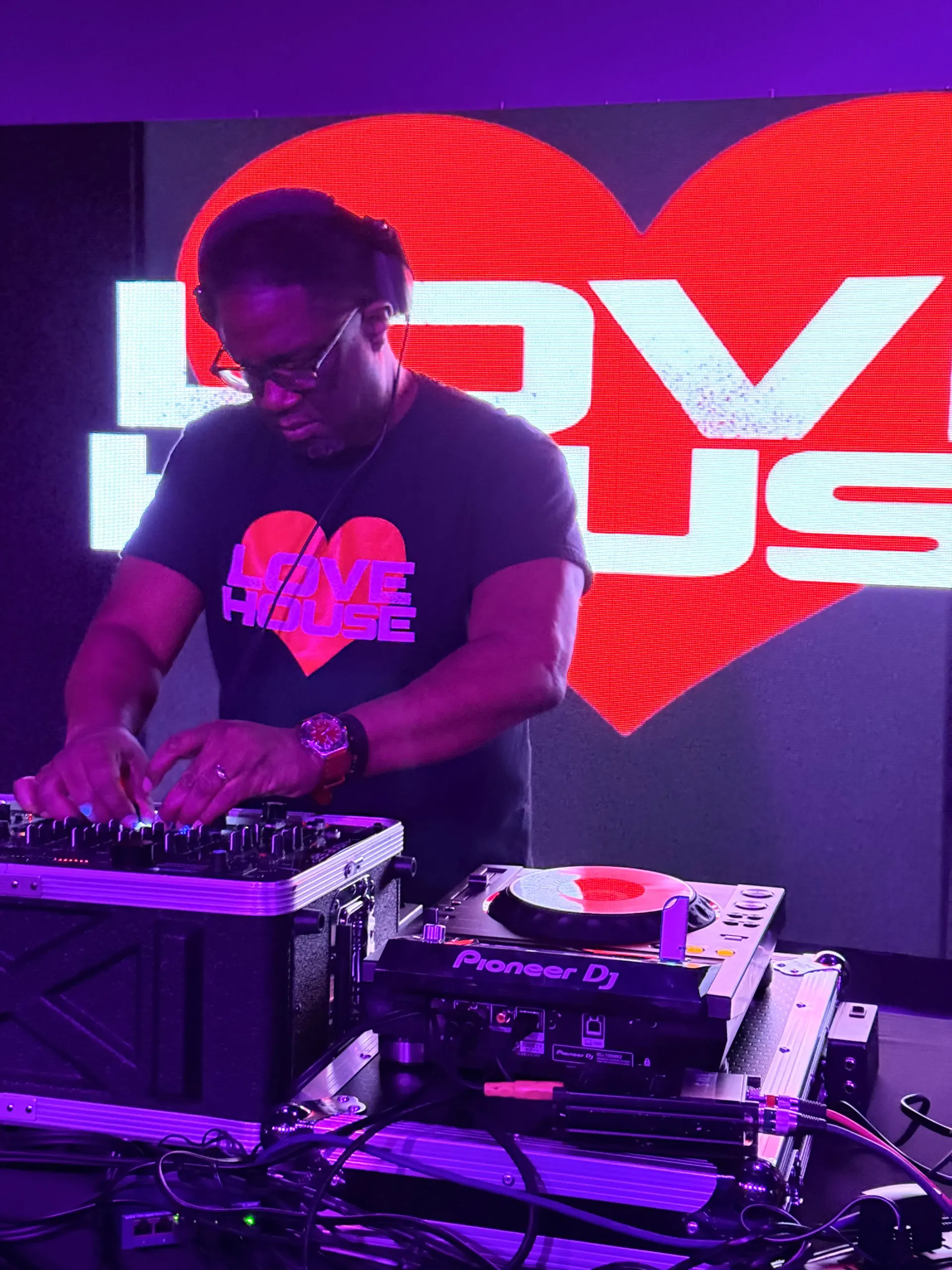 DJ performing a LoveHouse set on Pioneer decks in front of the LoveHouse heart backdrop.